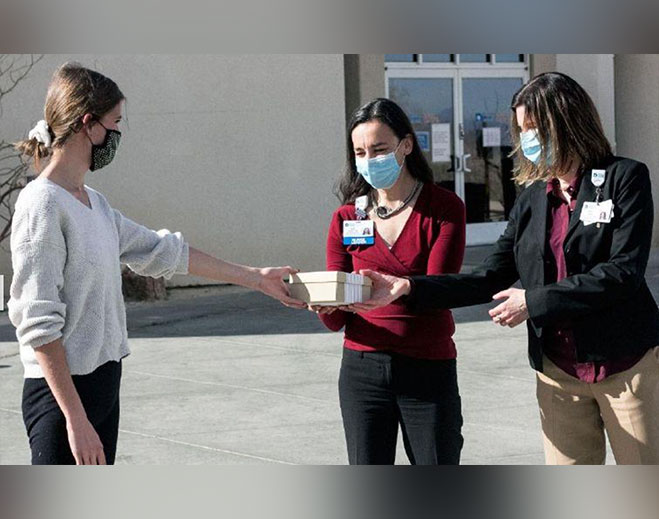Masked individuals exchanging food donation boxes outdoors